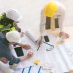 A top view of engineers and architects measuring and planning building blueprints on a construction site.