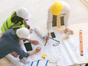 A top view of engineers and architects measuring and planning building blueprints on a construction site.