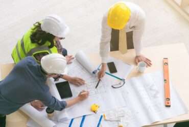 A top view of engineers and architects measuring and planning building blueprints on a construction site.