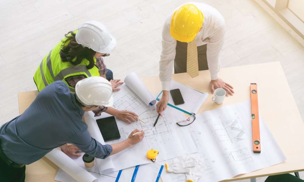 A top view of engineers and architects measuring and planning building blueprints on a construction site.