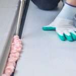 A person in on their hands and knees as they apply a sealant foam to the ground. The foam is bubbling and pink.