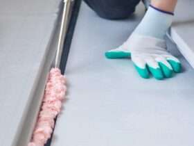 A person in on their hands and knees as they apply a sealant foam to the ground. The foam is bubbling and pink.
