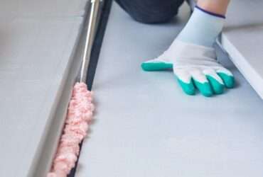 A person in on their hands and knees as they apply a sealant foam to the ground. The foam is bubbling and pink.