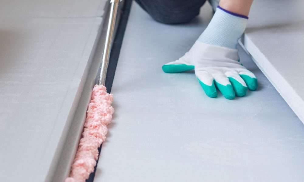 A person in on their hands and knees as they apply a sealant foam to the ground. The foam is bubbling and pink.