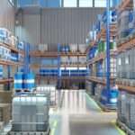 A warehouse aisle lined with metal racks holding blue barrels, gray containers, and pallets on a polished floor.