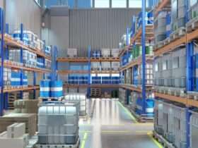 A warehouse aisle lined with metal racks holding blue barrels, gray containers, and pallets on a polished floor.