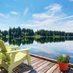 A small dock looking out over a calm lake. There are two yellow chairs on the dock, along with a small flower pot.
