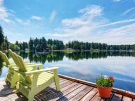 A small dock looking out over a calm lake. There are two yellow chairs on the dock, along with a small flower pot.