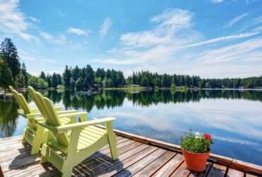 A small dock looking out over a calm lake. There are two yellow chairs on the dock, along with a small flower pot.