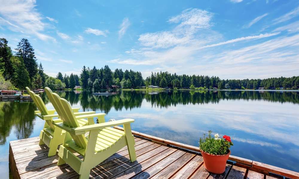 A small dock looking out over a calm lake. There are two yellow chairs on the dock, along with a small flower pot.