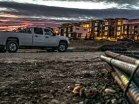 A truck is parked in the middle of a dirt road. There is an apartment building in the background.