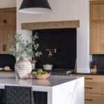 A modern kitchen with rustic wooden cabinets and a black backsplash. There is also an island with a flower vase on it.