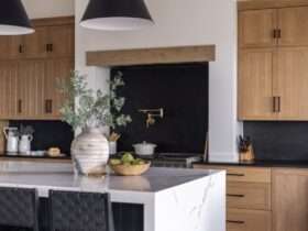 A modern kitchen with rustic wooden cabinets and a black backsplash. There is also an island with a flower vase on it.