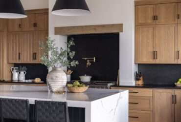 A modern kitchen with rustic wooden cabinets and a black backsplash. There is also an island with a flower vase on it.