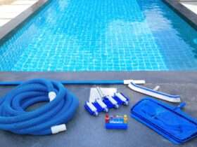 A close-up of a swimming pool with maintenance equipment lining one side. There's a brush, a net, tubing, and a water testing kit.