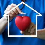 A person wearing blue scrubs is holding a cartoon heart in their left hand and is holding a stethoscope in their right.