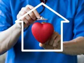 A person wearing blue scrubs is holding a cartoon heart in their left hand and is holding a stethoscope in their right.