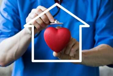 A person wearing blue scrubs is holding a cartoon heart in their left hand and is holding a stethoscope in their right.