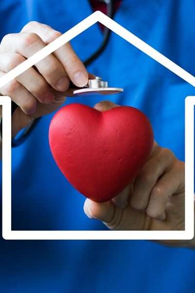 A person wearing blue scrubs is holding a cartoon heart in their left hand and is holding a stethoscope in their right.
