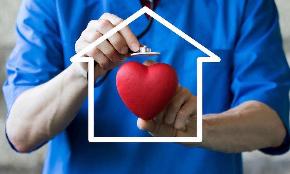 A person wearing blue scrubs is holding a cartoon heart in their left hand and is holding a stethoscope in their right.