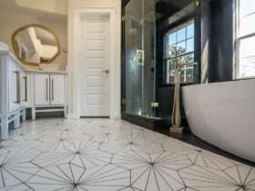 Black and white bathroom with hexagon floor tile, glass shower, vanity, and mirror viewed from a low angle.