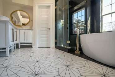 Black and white bathroom with hexagon floor tile, glass shower, vanity, and mirror viewed from a low angle.
