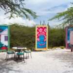 a series of colorful artwork in tall canvases forming a half-circle outdoors, surrounded by greenery and chairs.