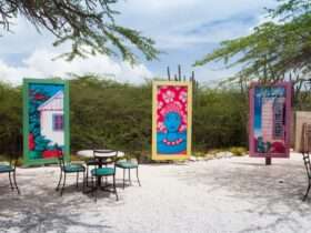 a series of colorful artwork in tall canvases forming a half-circle outdoors, surrounded by greenery and chairs.
