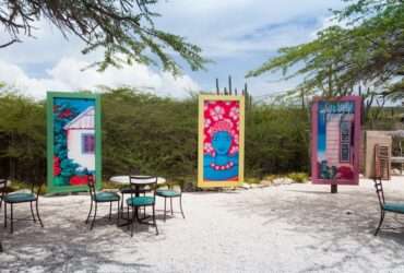 a series of colorful artwork in tall canvases forming a half-circle outdoors, surrounded by greenery and chairs.
