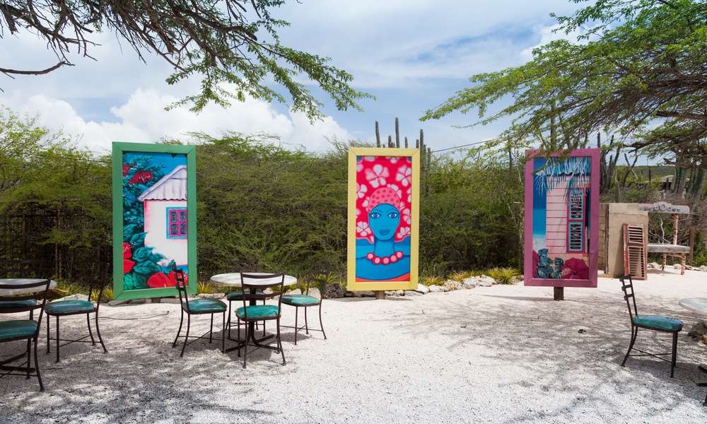 a series of colorful artwork in tall canvases forming a half-circle outdoors, surrounded by greenery and chairs.