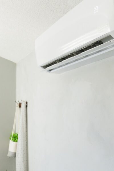 A man in a blue shirt stands indoors, holding his hand to his head, staring at an air conditioner on the wall.