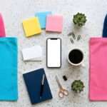 A collection of company swag sits on a white surface. There are tote bags, notebooks, pens, and note pads.
