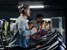 A man wearing headphones running on a treadmill in a gym beside other people using exercise machines.