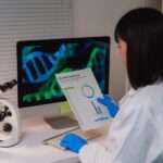 A female lab scientist at the work desk in front of a monitor, reading the results to the lab test she ran.