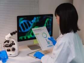 A female lab scientist at the work desk in front of a monitor, reading the results to the lab test she ran.