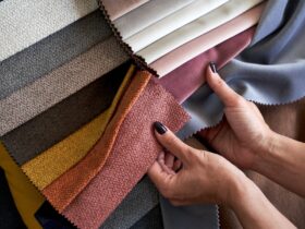 A person compares colorful upholstery fabric swatches in gray, pink, orange, yellow, brown, and neutral tones.