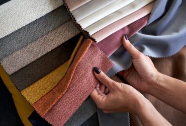 A person compares colorful upholstery fabric swatches in gray, pink, orange, yellow, brown, and neutral tones.