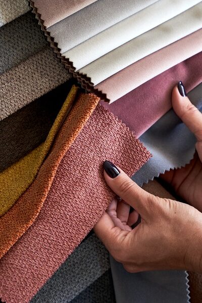A person compares colorful upholstery fabric swatches in gray, pink, orange, yellow, brown, and neutral tones.