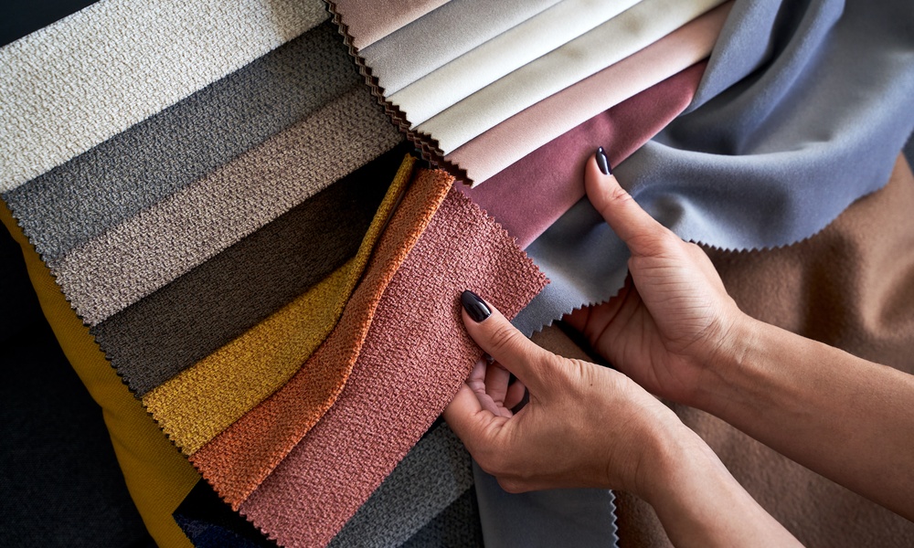 A person compares colorful upholstery fabric swatches in gray, pink, orange, yellow, brown, and neutral tones.