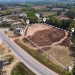 An aerial view of an open plot of land in a neighborhood. The plot is outlined by a dotted white line.