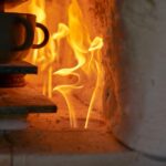 A stack of ceramic cups sit on a flat surface inside a kiln that has a fire going. The flames are orange.
