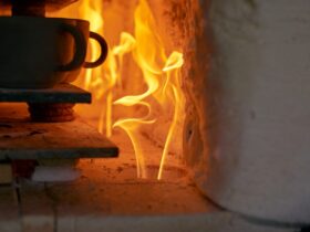 A stack of ceramic cups sit on a flat surface inside a kiln that has a fire going. The flames are orange.