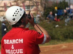 A person is holding a walkie-talkie up to their mouth. The back of the shirt reads "search and rescue."
