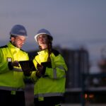 Two people are standing next to each other, one man and one woman. They are both wearing hi-vis jackets.