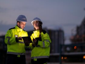 Two people are standing next to each other, one man and one woman. They are both wearing hi-vis jackets.
