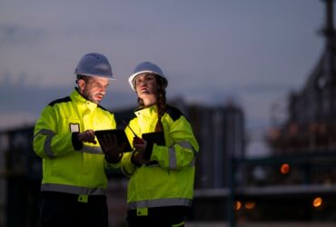 Two people are standing next to each other, one man and one woman. They are both wearing hi-vis jackets.