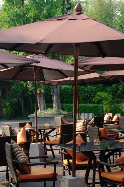 Multiple tables and chairs with orange cushions in an outdoor space under brown umbrellas with metal bases.Multiple tables and chairs with orange cushions in an outdoor space under brown umbrellas with metal bases.