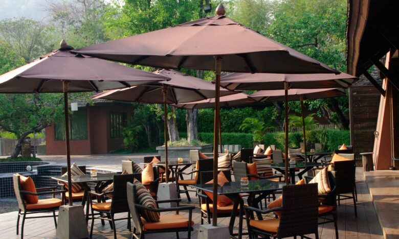 Multiple tables and chairs with orange cushions in an outdoor space under brown umbrellas with metal bases.Multiple tables and chairs with orange cushions in an outdoor space under brown umbrellas with metal bases.