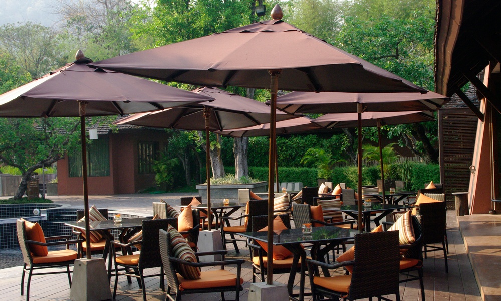 Multiple tables and chairs with orange cushions in an outdoor space under brown umbrellas with metal bases.Multiple tables and chairs with orange cushions in an outdoor space under brown umbrellas with metal bases.