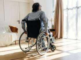 A man in a wheelchair moving towards the large windows within his living room. The space also has a couch.